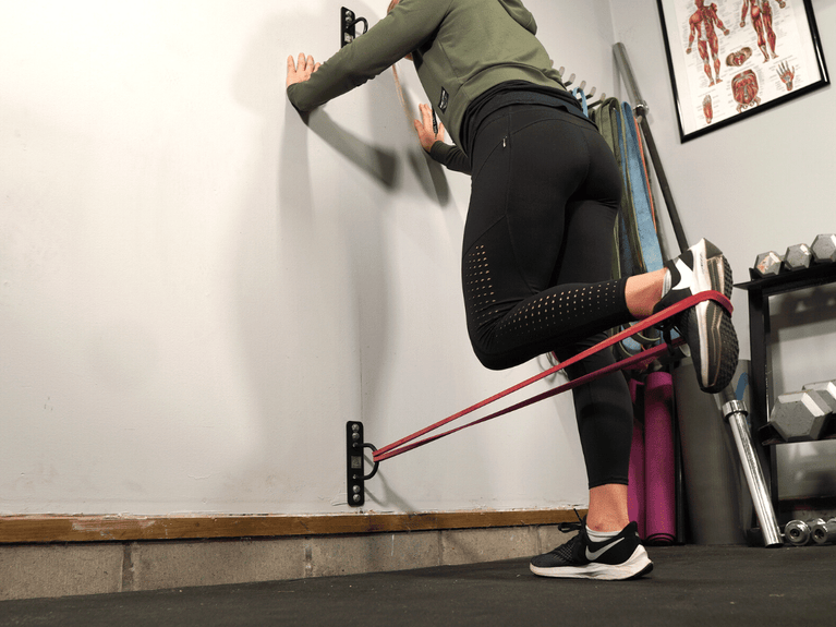 Single-leg hamstring curl with resistance bands, supported by a wall anchor for effective leg conditioning